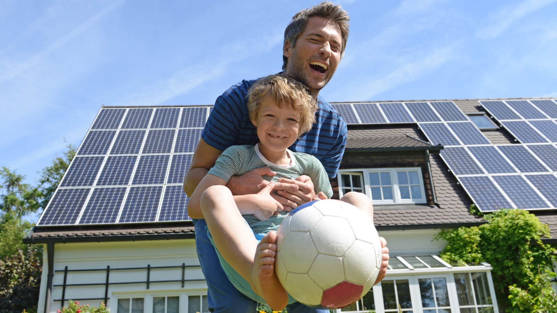 Son and father playing in front of their house with solar panels