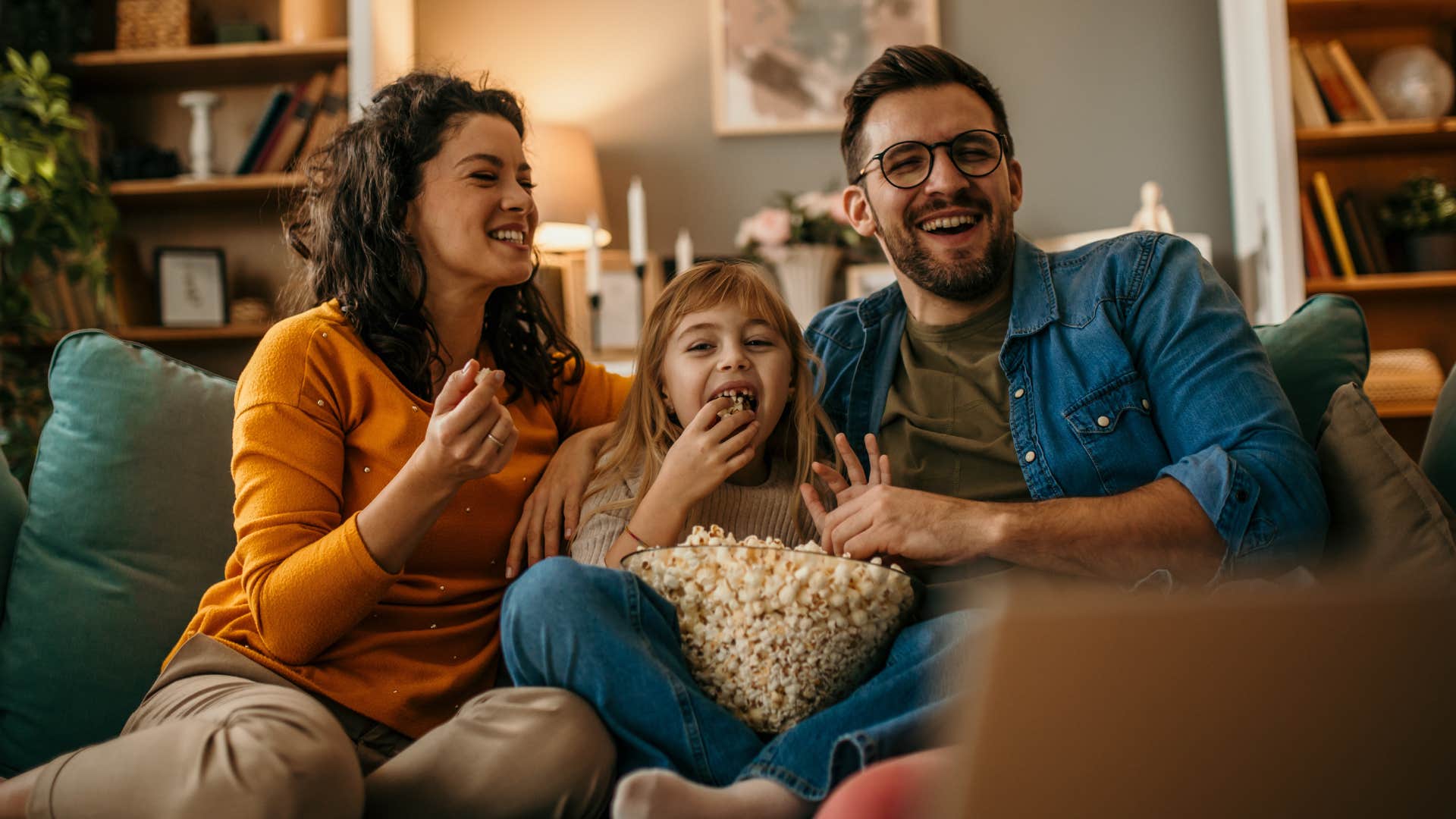 Family smiling and eating popcorn on their couch together