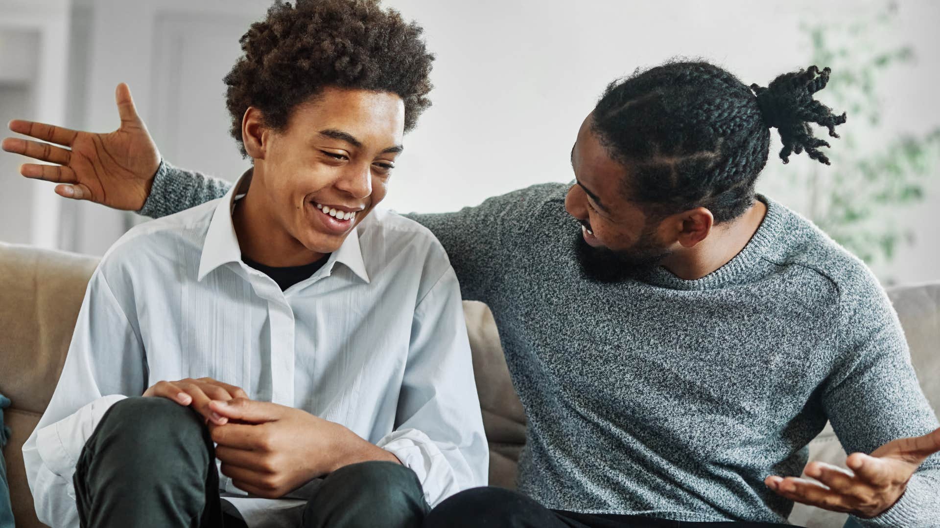 Teenage boy smiling while sitting next to his dad.