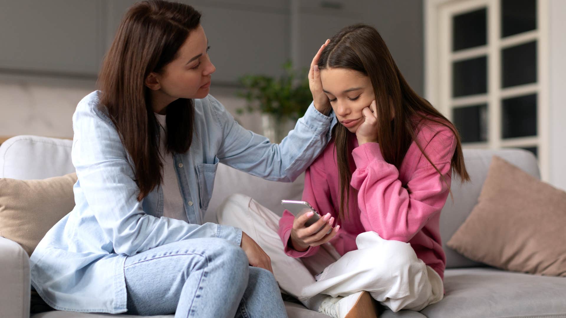 Woman comforting her sad teenage daughter on her phone.