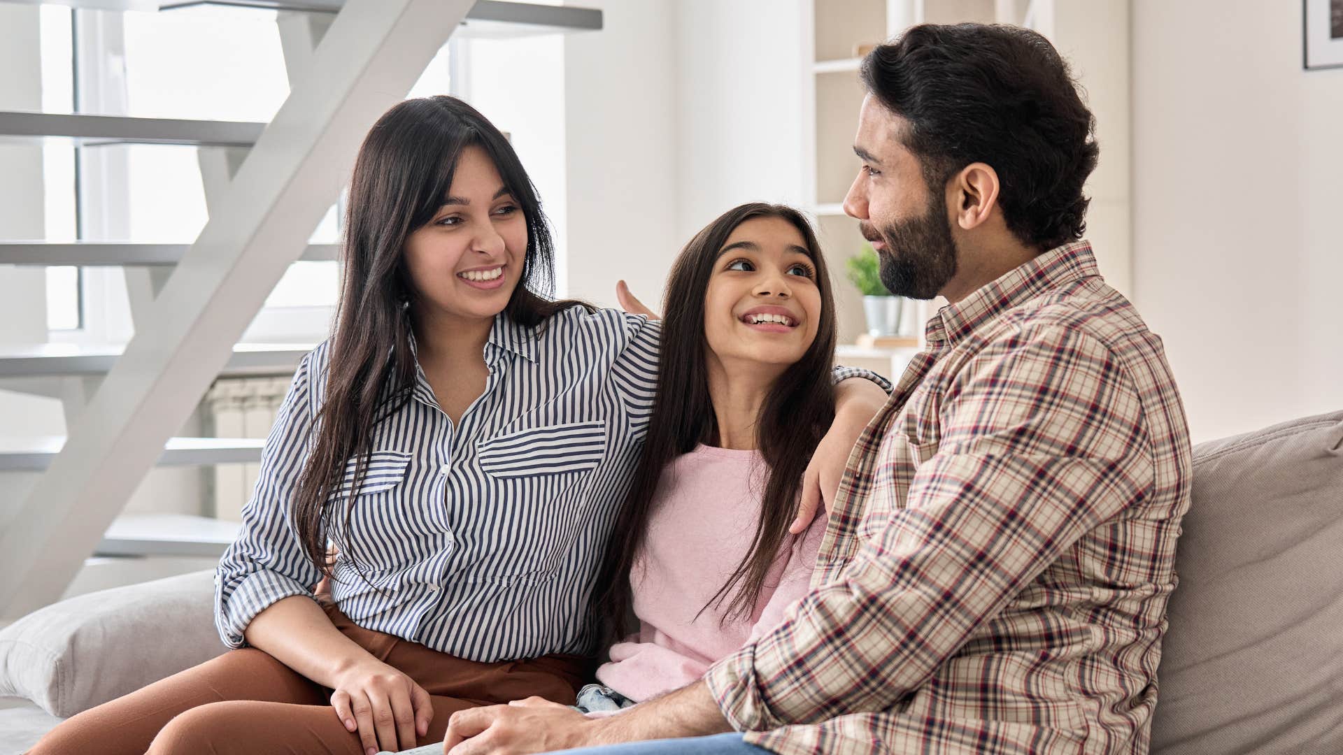 Two parents smiling and talking to their young daughter.