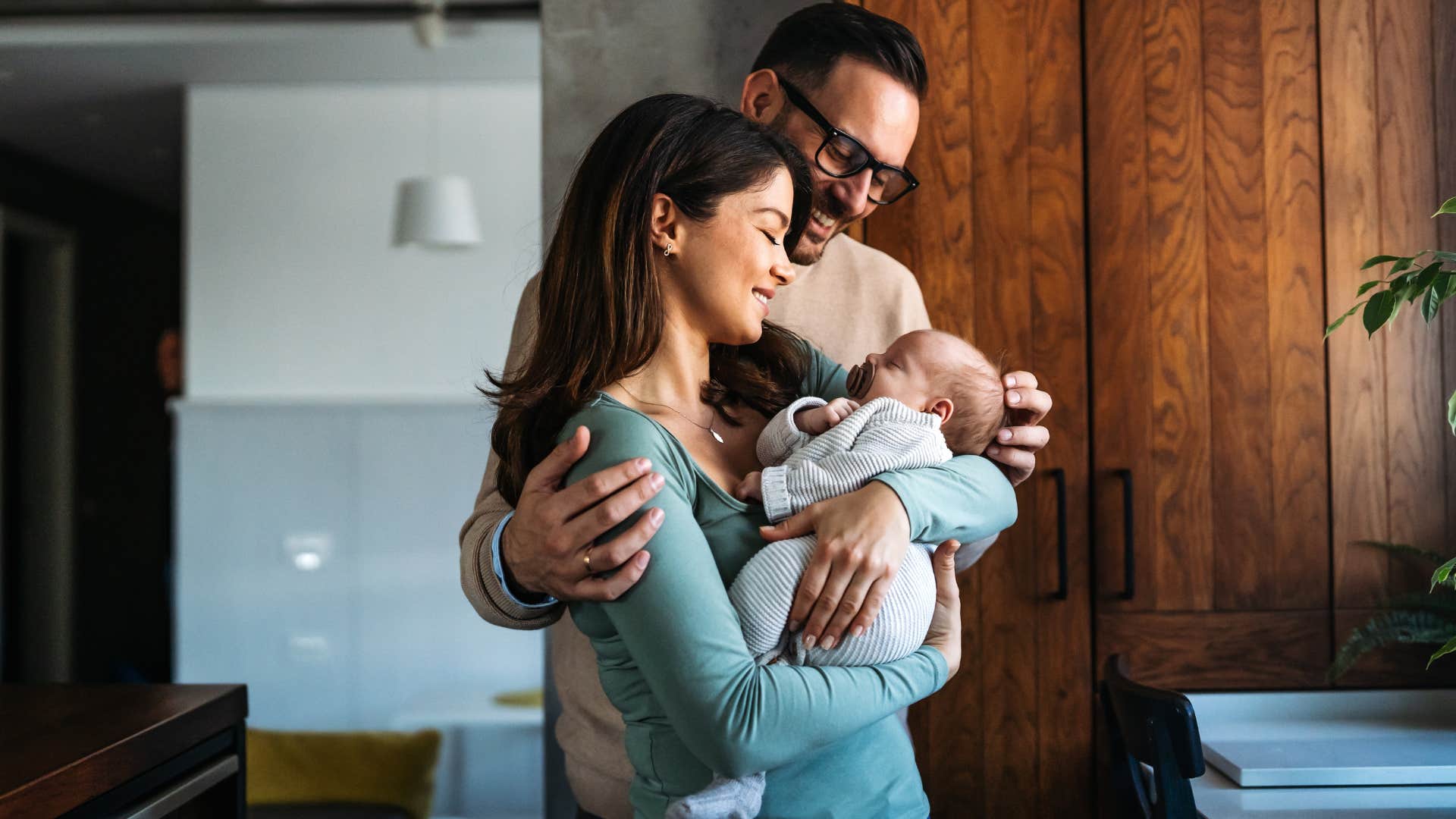 Two parents smiling and holding their newborn.