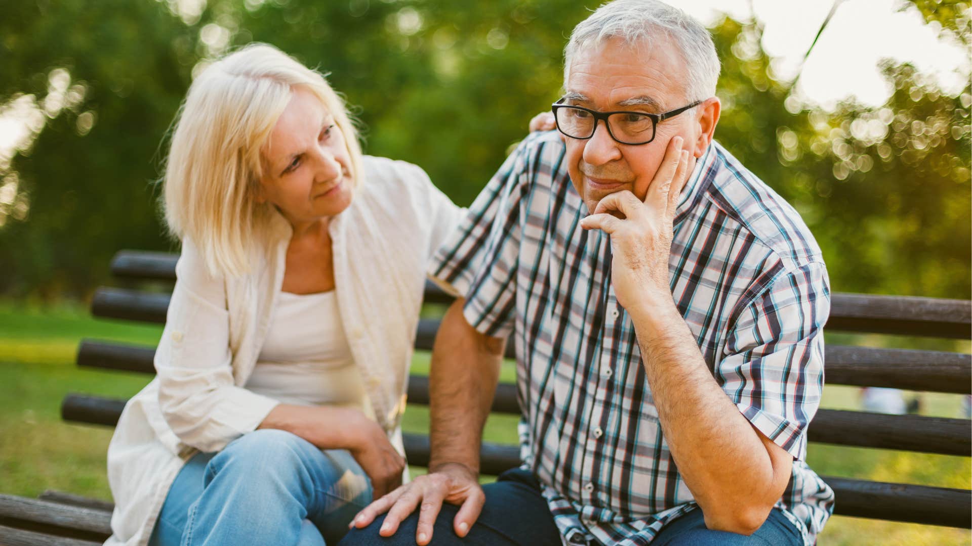 Woman comforting her older husband on a park bench. 