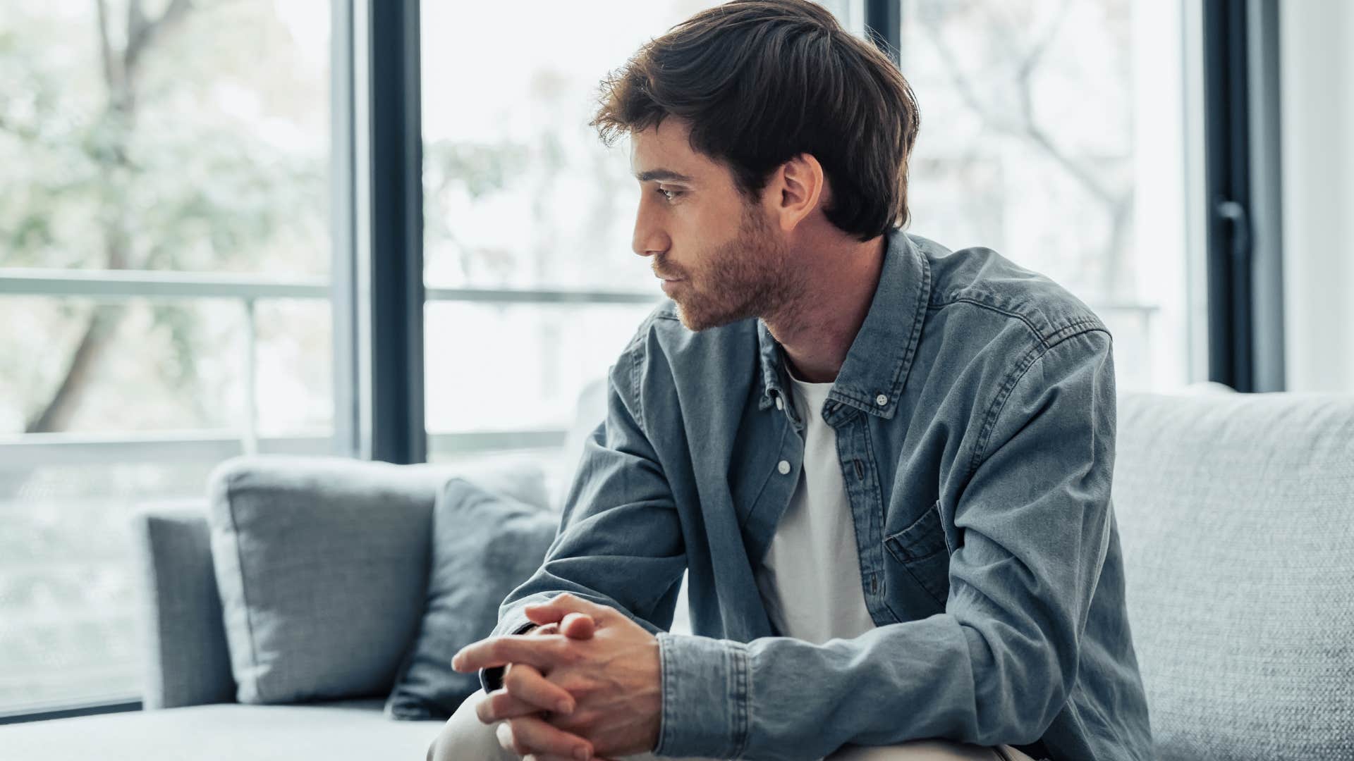 Man looking sad sitting in front of a window.