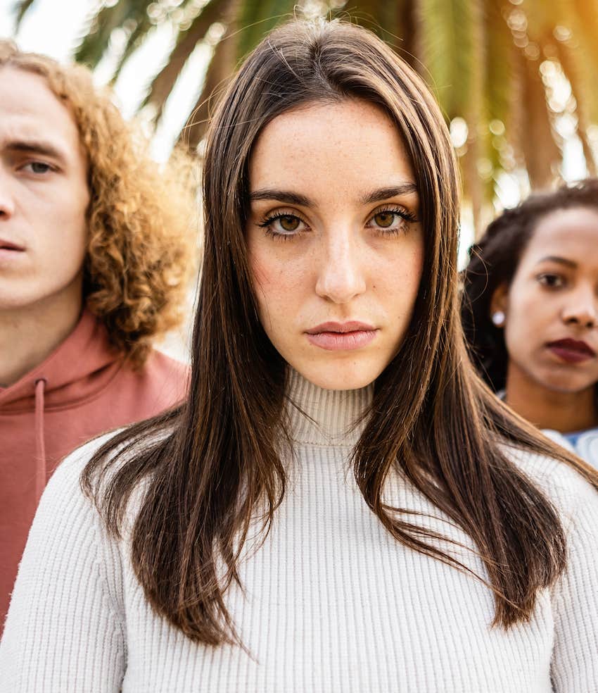 Serious woman stands with two people behind her