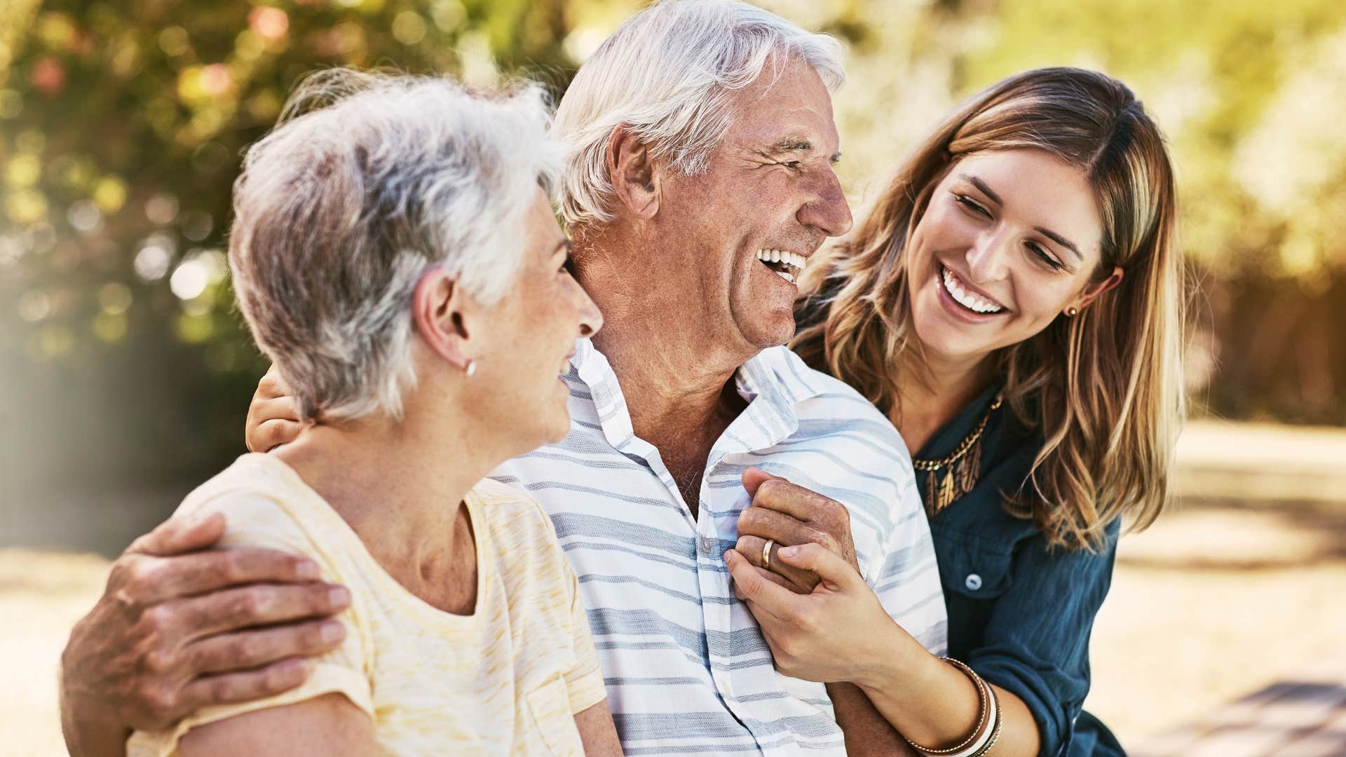 Adult daughter smiling and hugging her mom and dad.