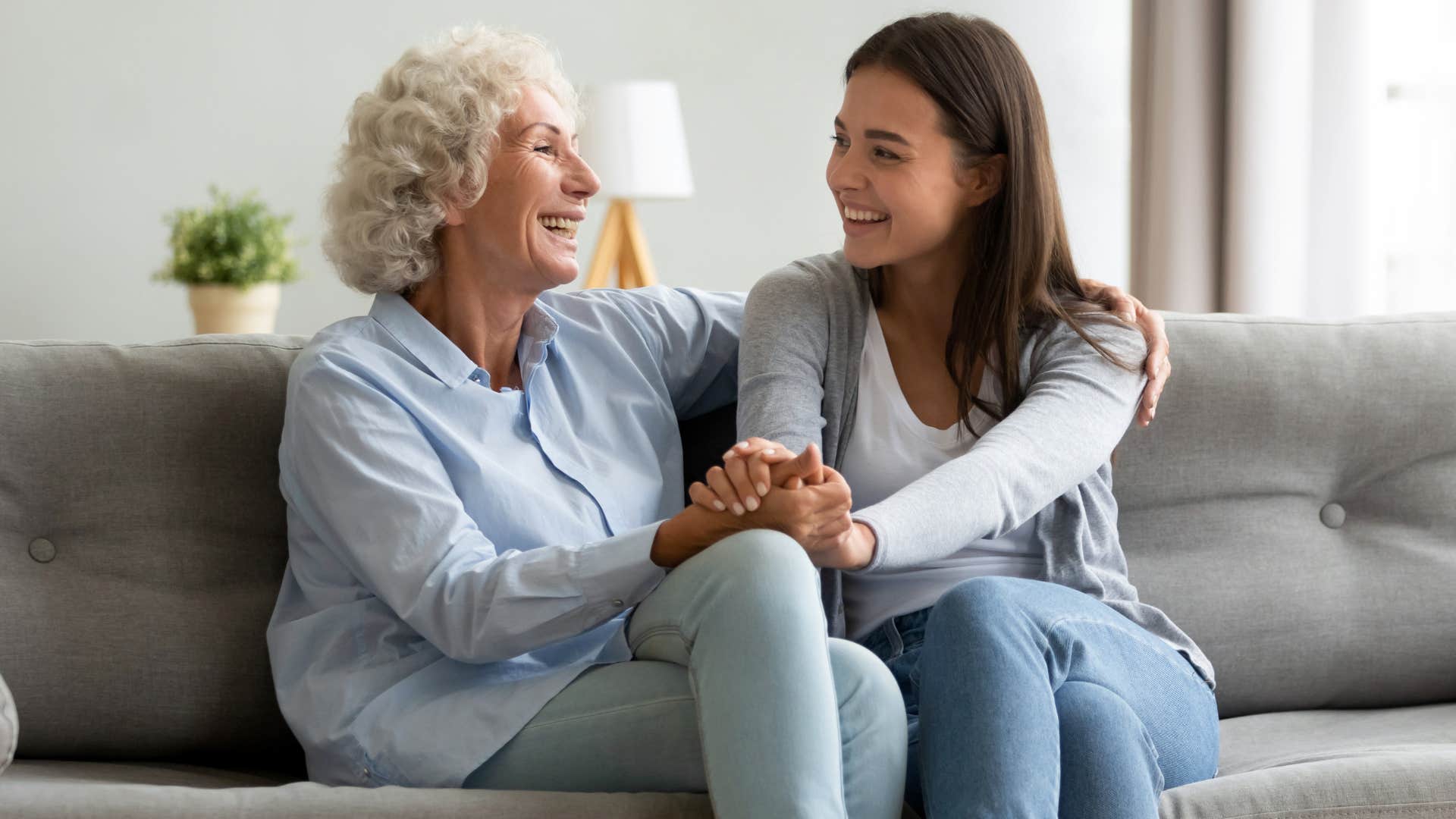 Adult daughter smiling while talking with her mother on the couch.