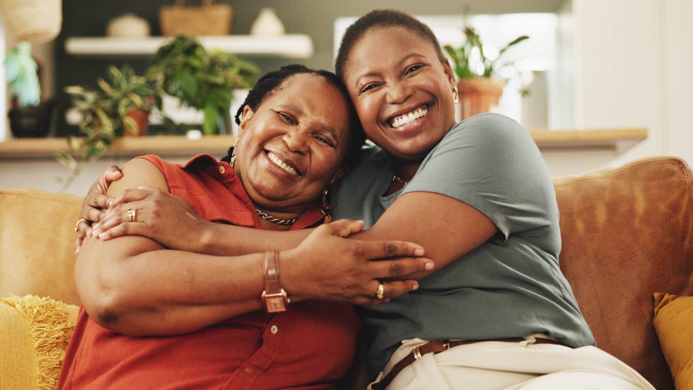 adult daughter smiling while hugging her mother on a couch