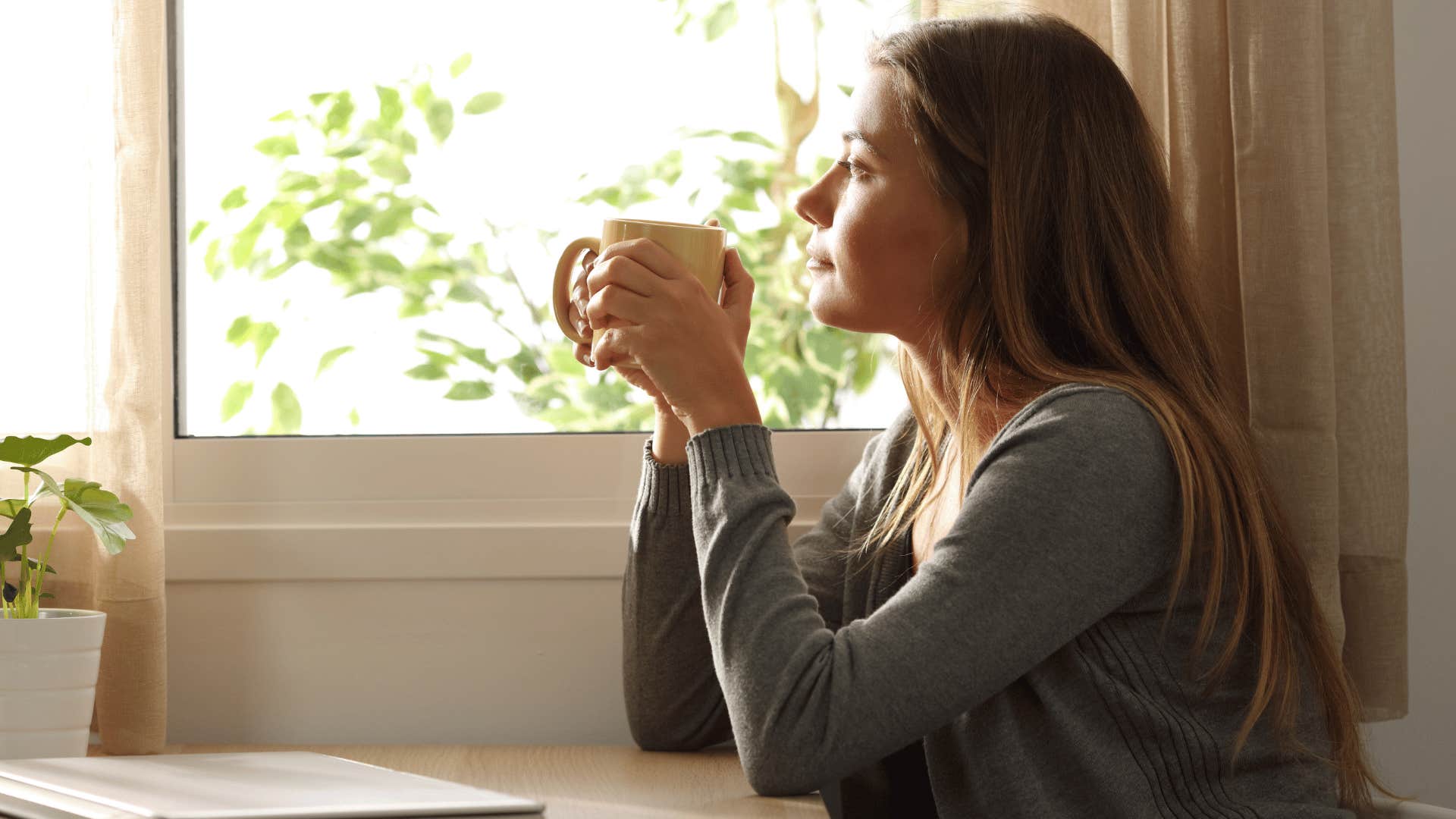 woman drinking coffee and staring out the window