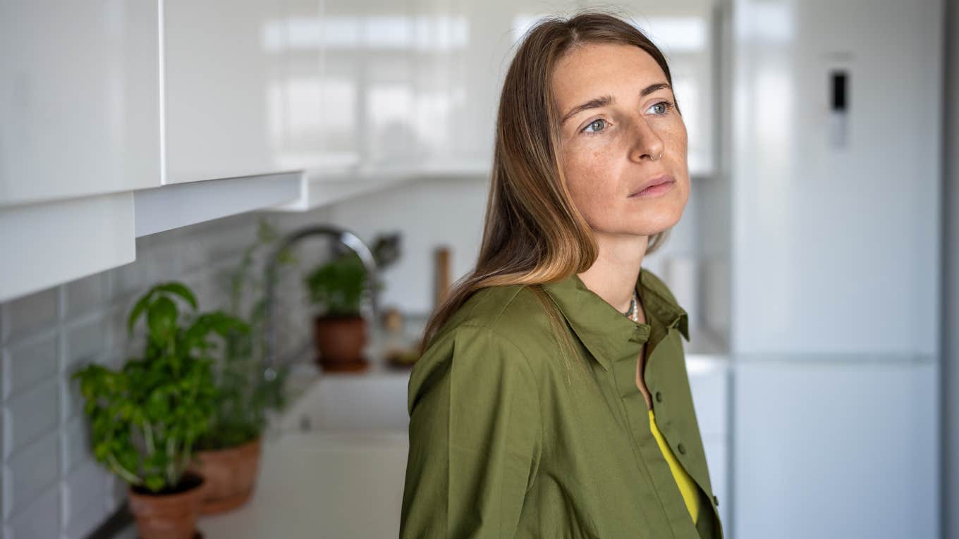 Pensive thoughtful woman with distressed mood stands in kitchen of home