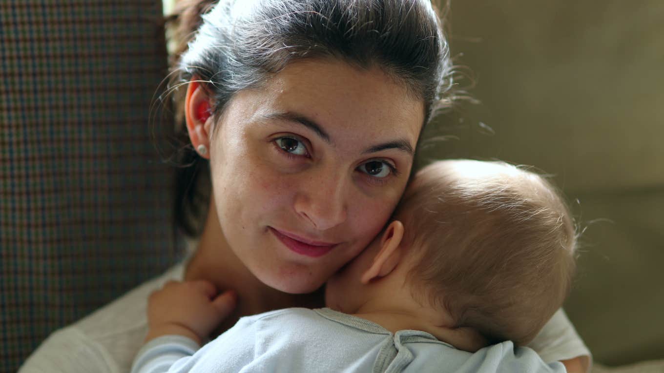 casual mom looking to camera holding sleeping infant