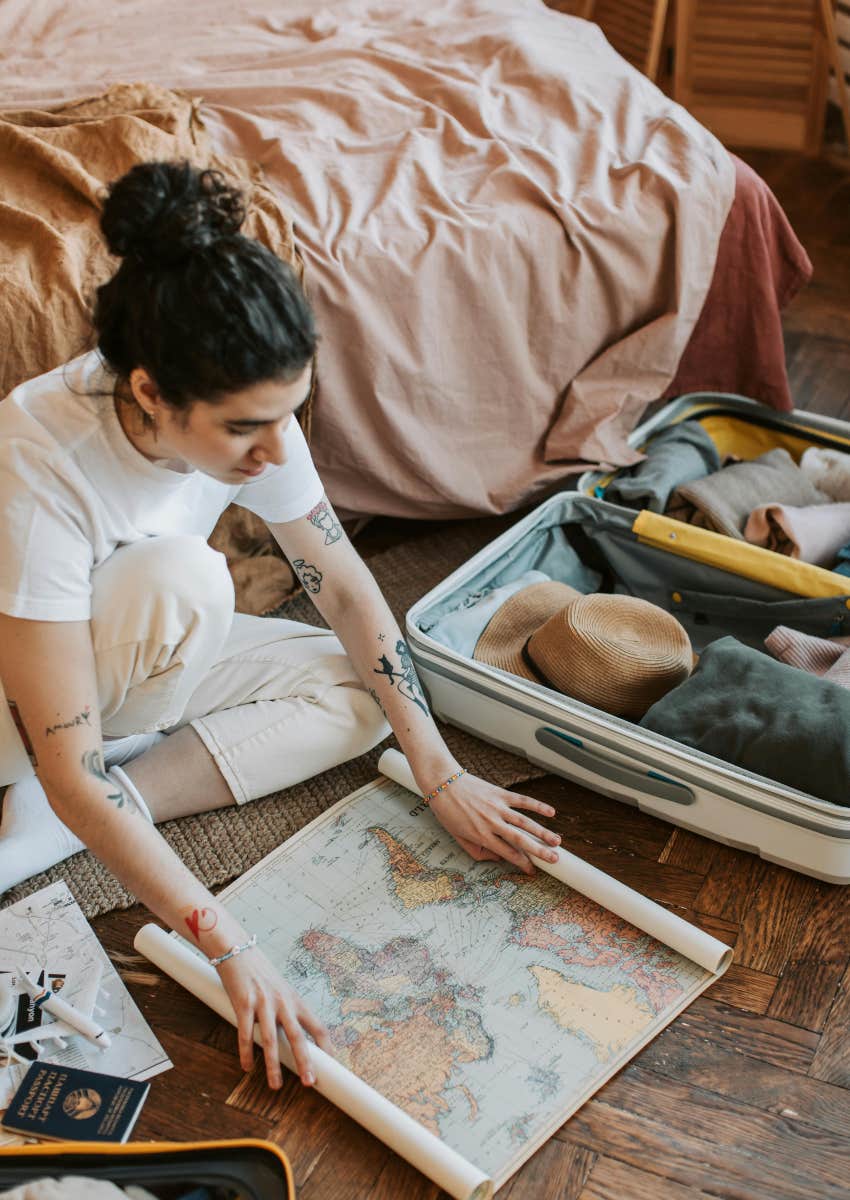 woman sitting on bedroom floor with map and packed suitcase