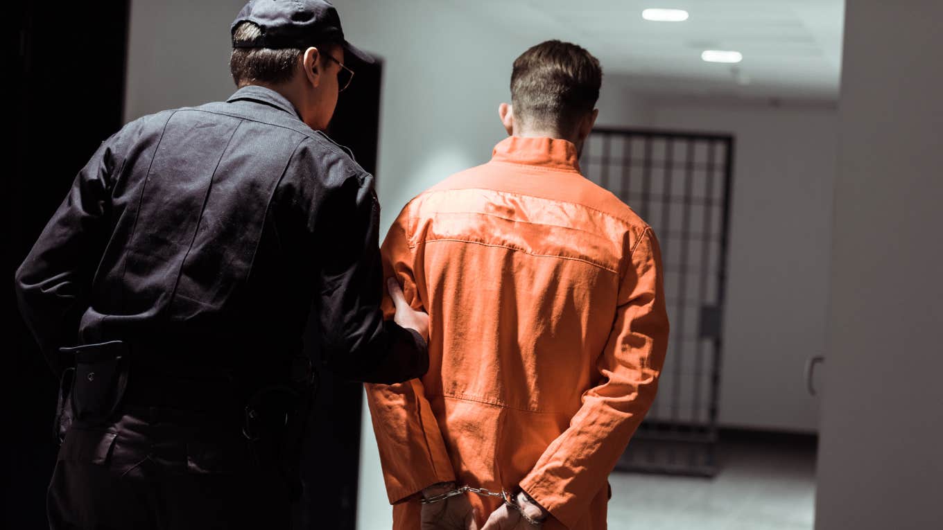 rear view of prison officer leading prisoner in handcuffs in corridor