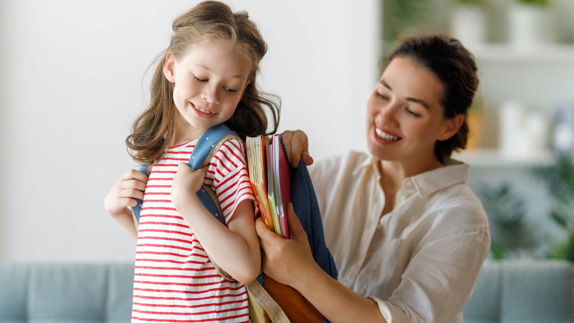 Mom putting her backpack on her young daughter.