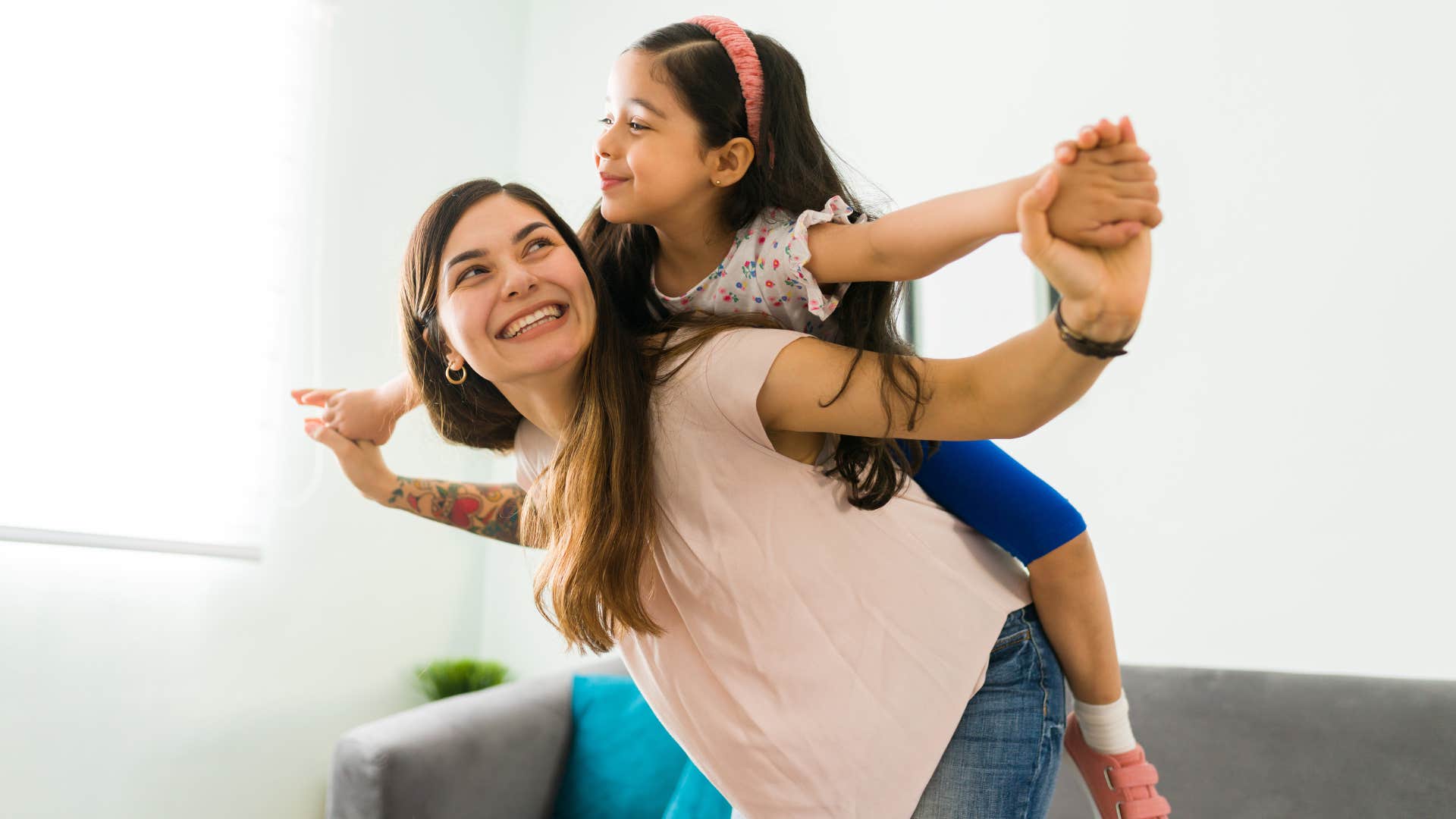 Mom smiling and holding her young daughter above her head.