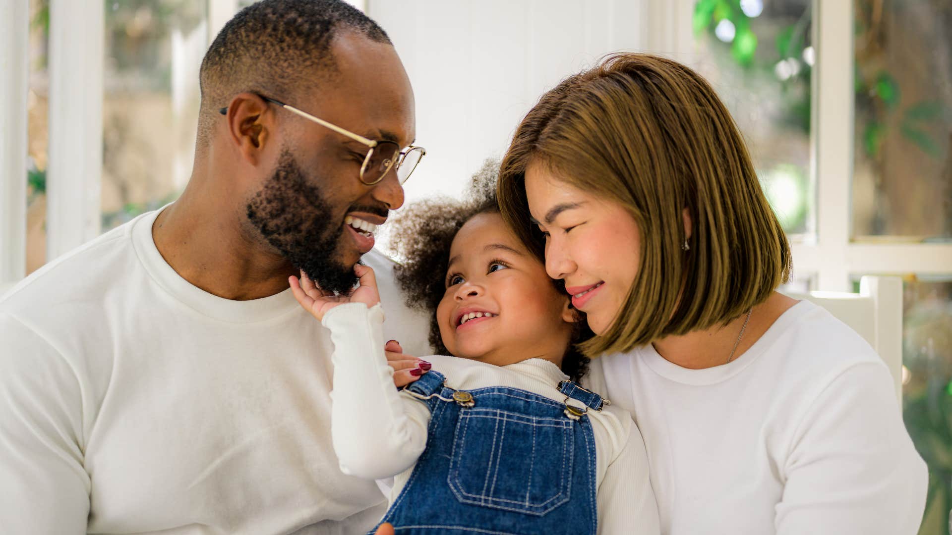 Parents hugging and smiling at their young daughter.