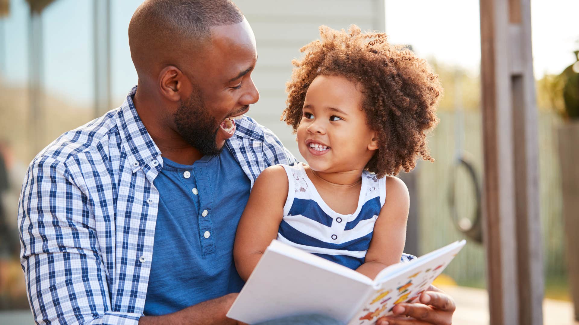 Dad smiling and reading a book with his daughter.