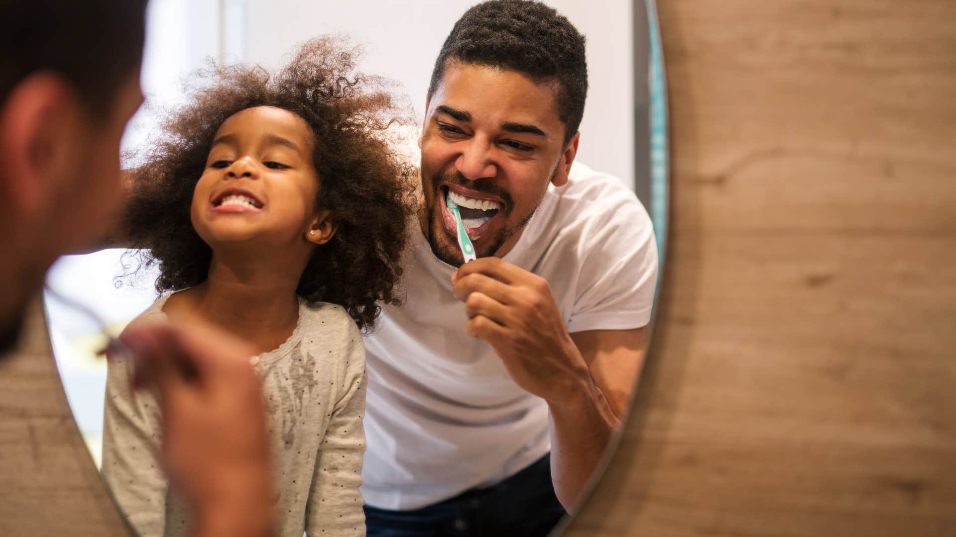 Man brushing his teeth with his daughter in the mirror.