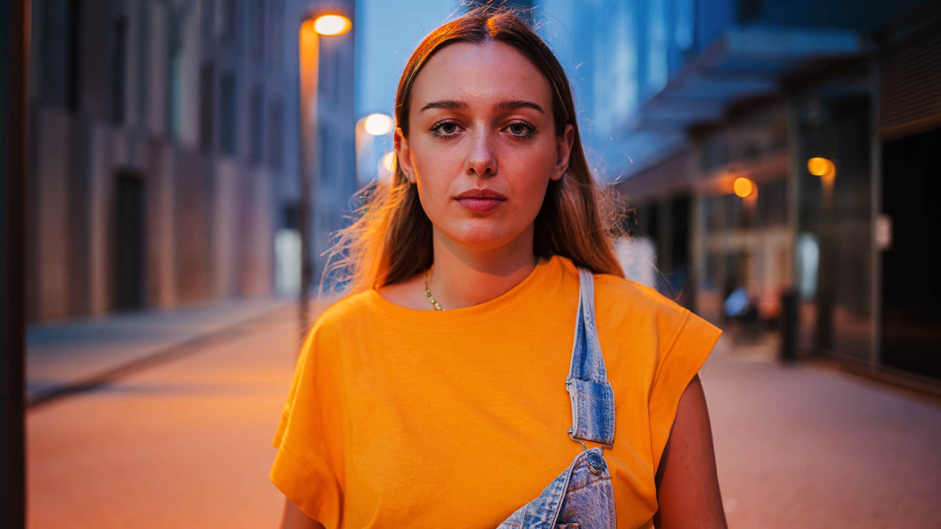 Individual portrait of serious young caucasian female standing outside at the night. 