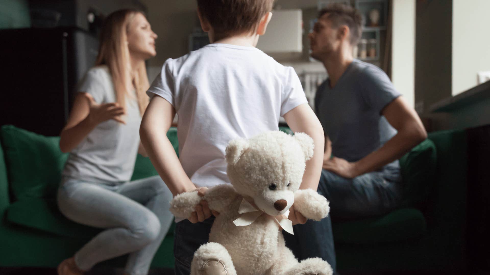 kid holding bear while parents argue