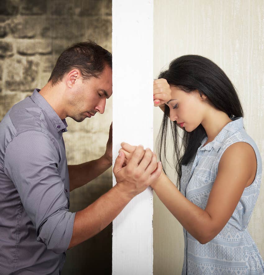 Broken -hearted man and woman hold hands on opposite side of a wall