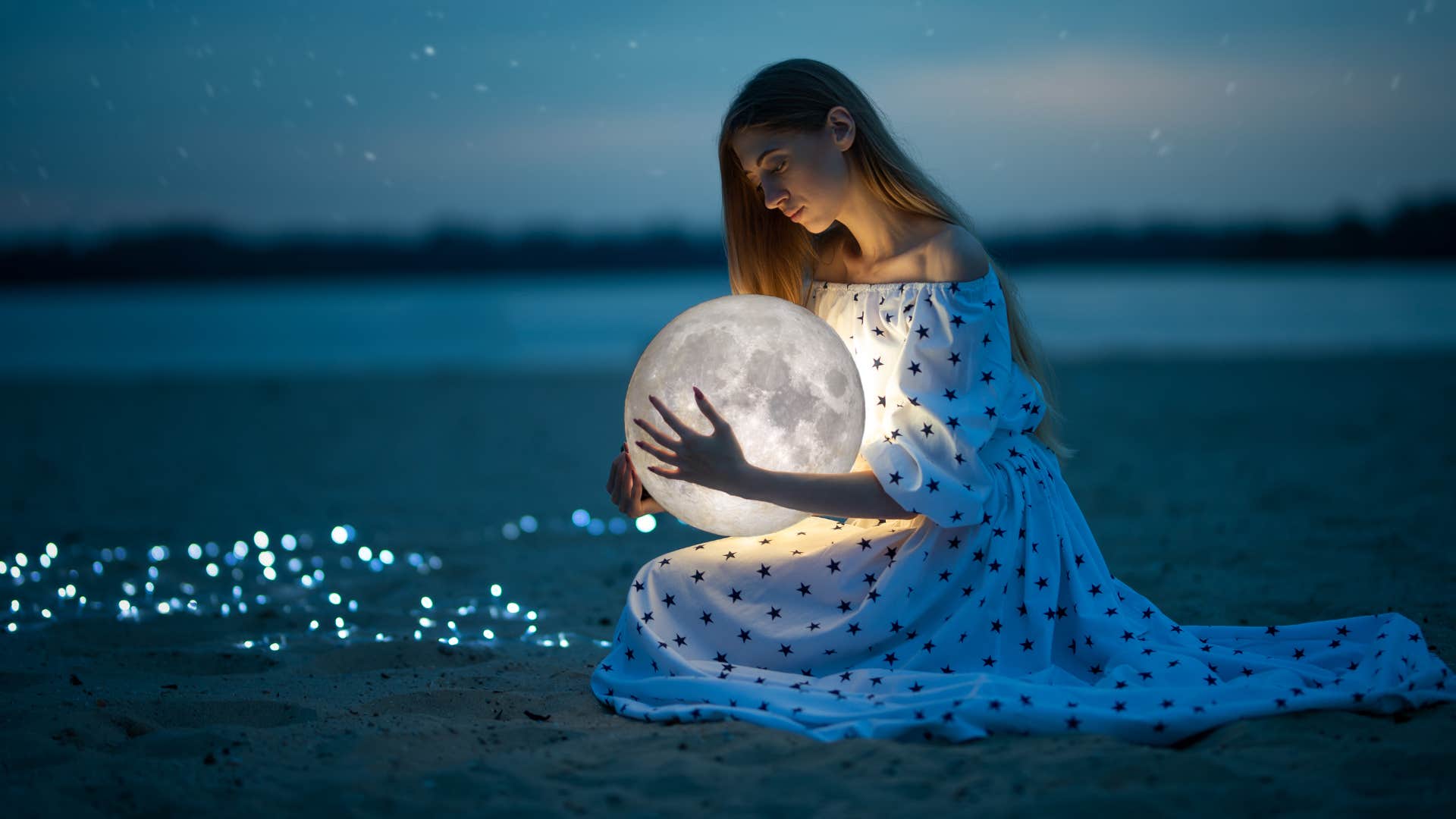 woman on a night beach with sand and stars hugs the moon.