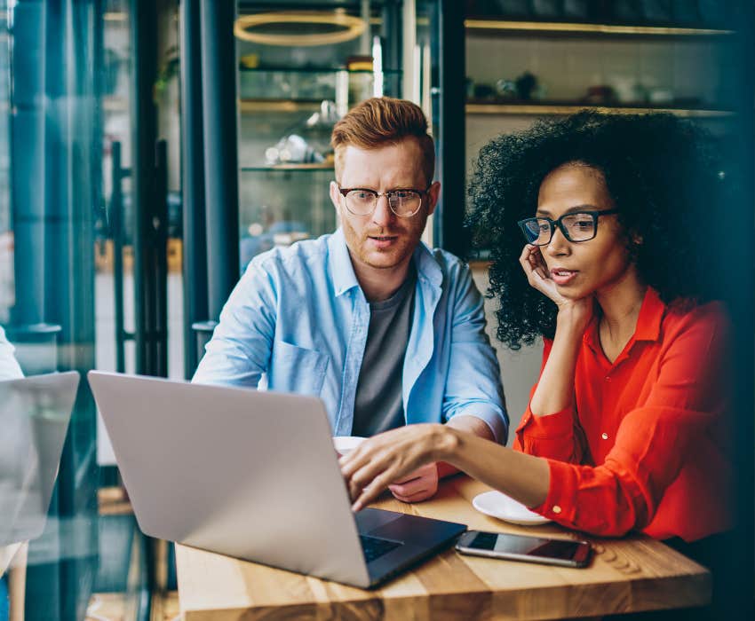 woman pointing on laptop and explaining task to colleague during meeting in coffee shop.