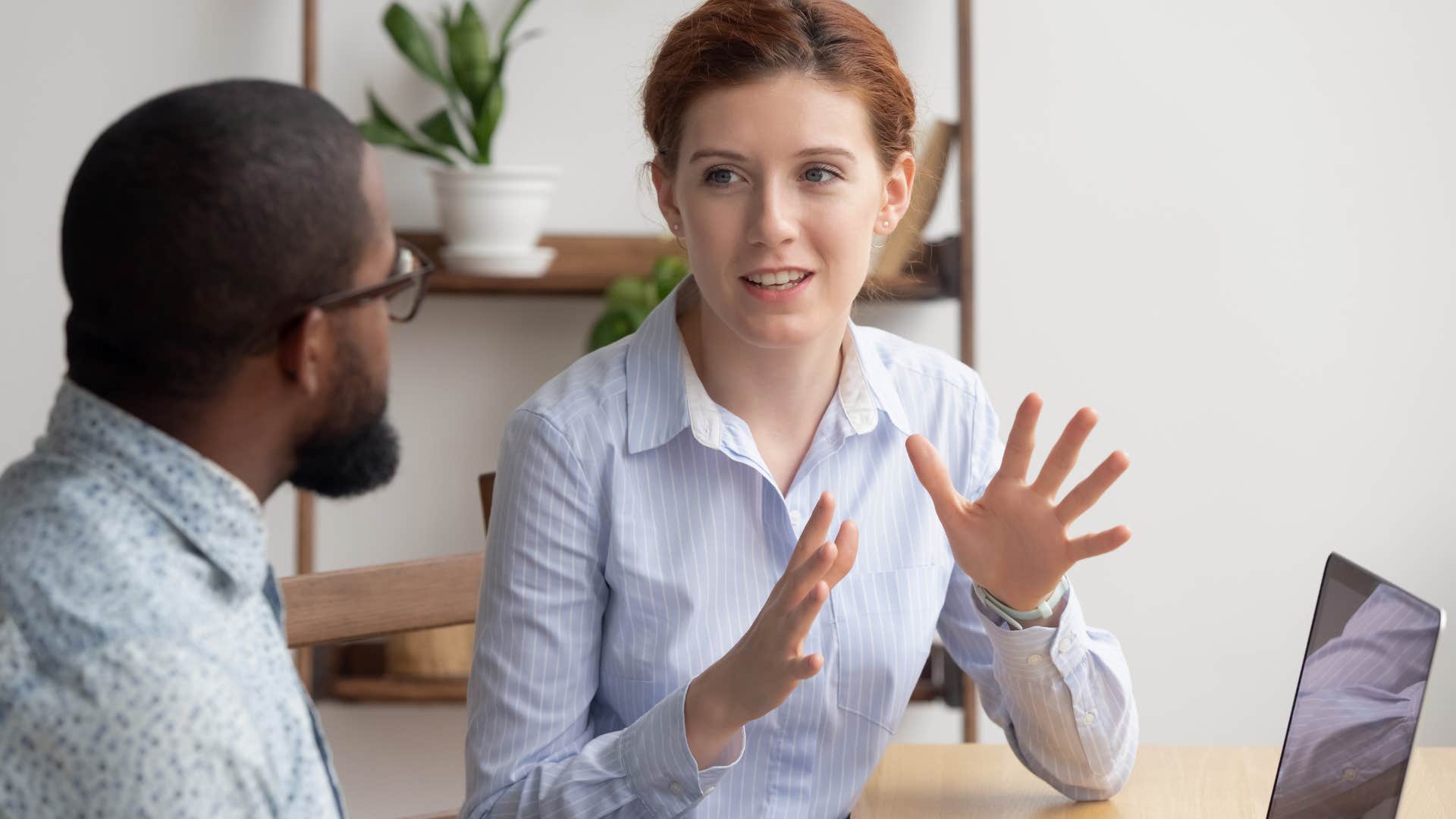 Woman holding her hands up while talking to a man at work