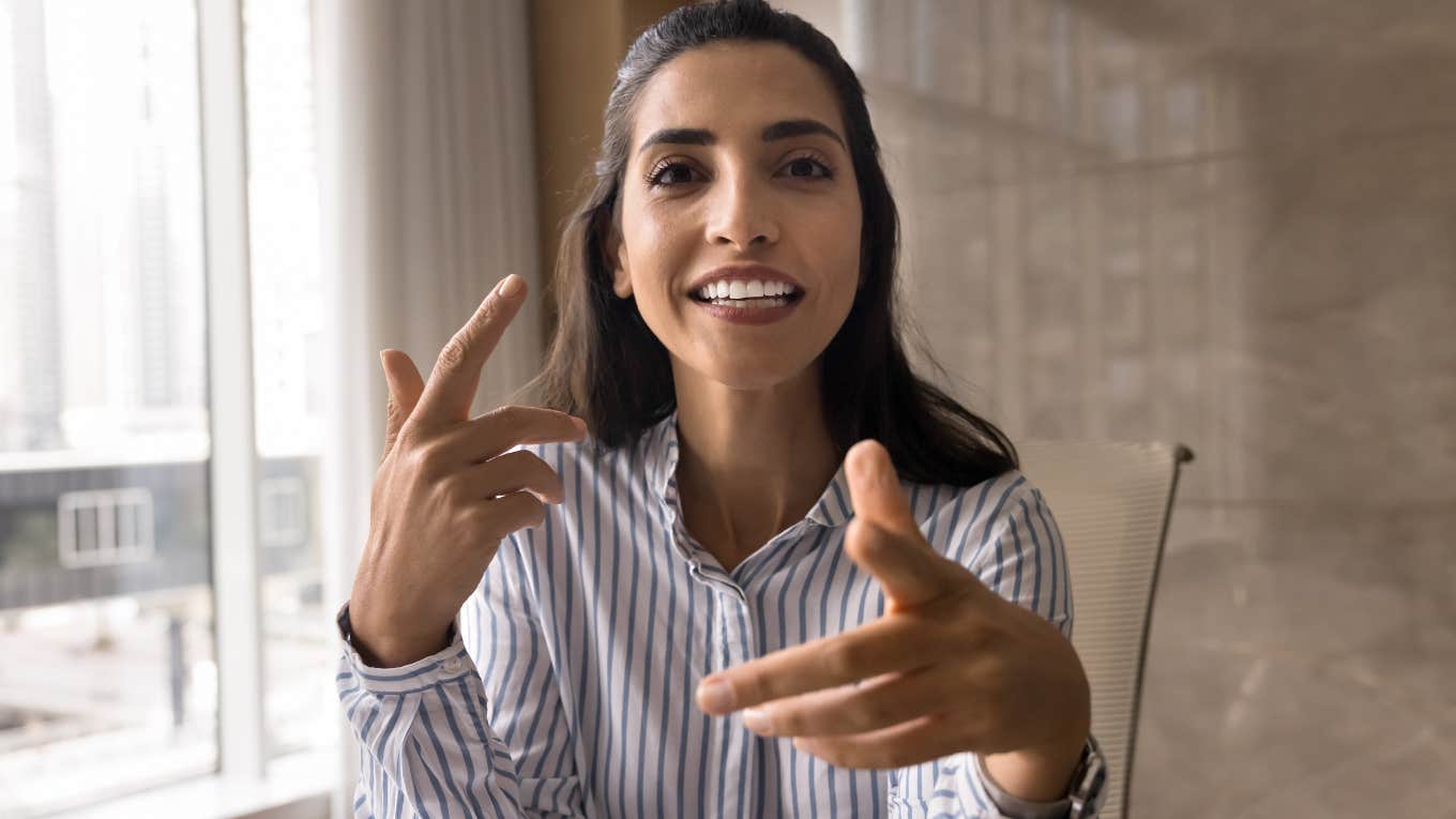 Smiling woman talking to someone behind the camera with her hands.