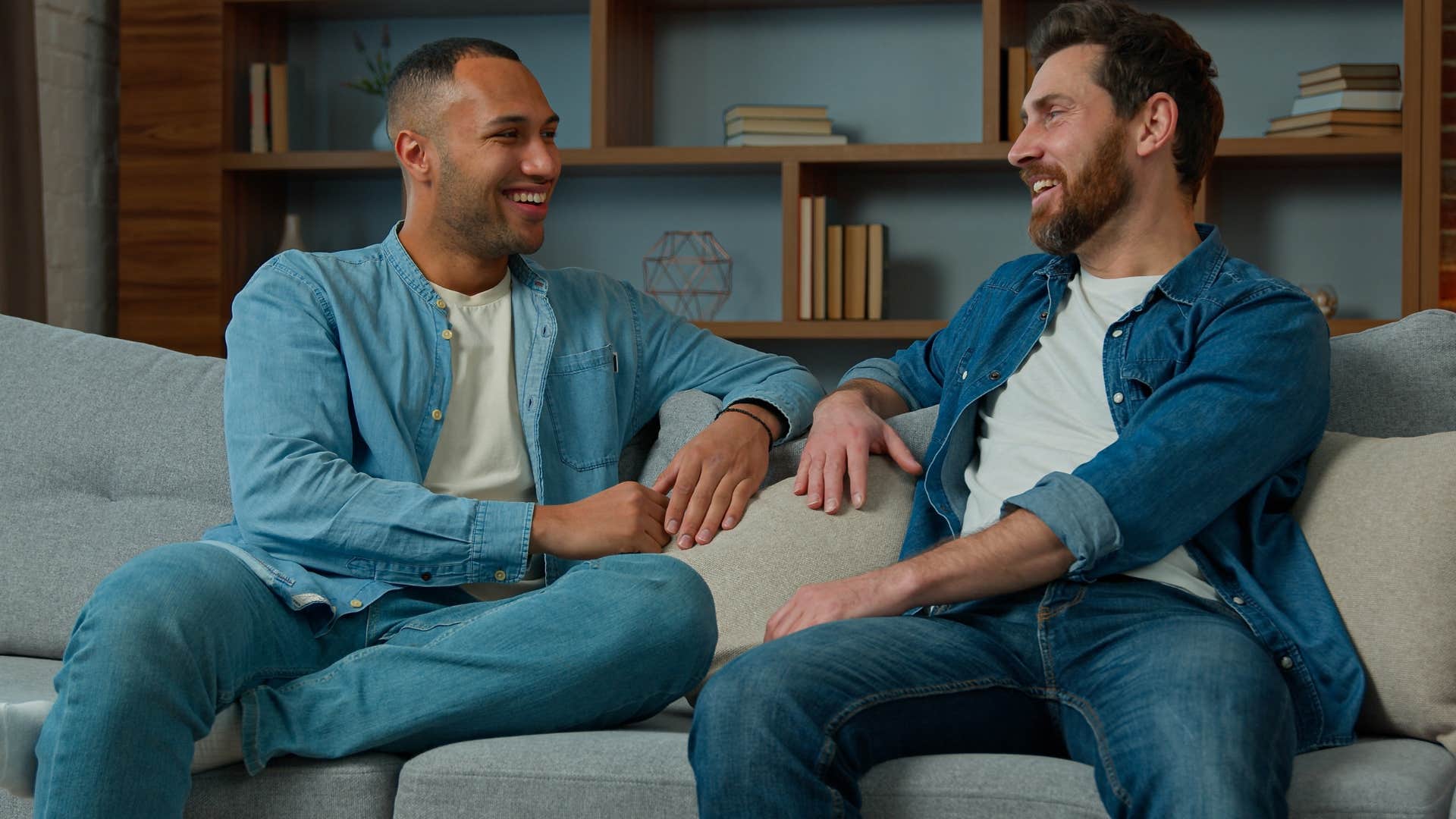 Two men smiling and talking to each other on a couch