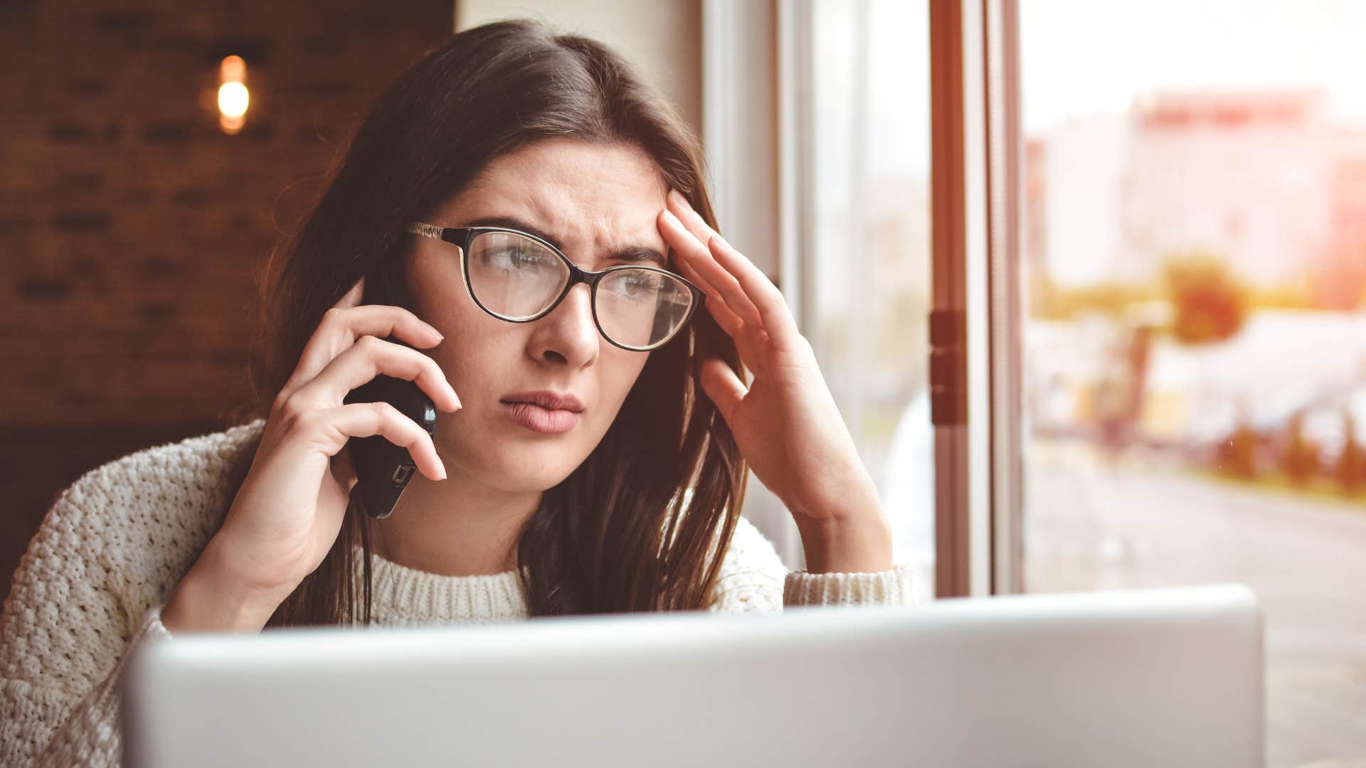 Woman holding her head while talking on the phone.