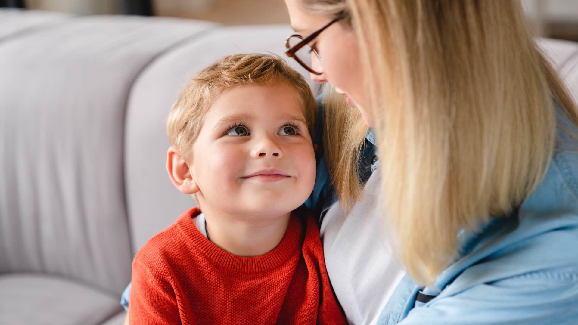 Caring young mother embracing toddler son sitting at home together.