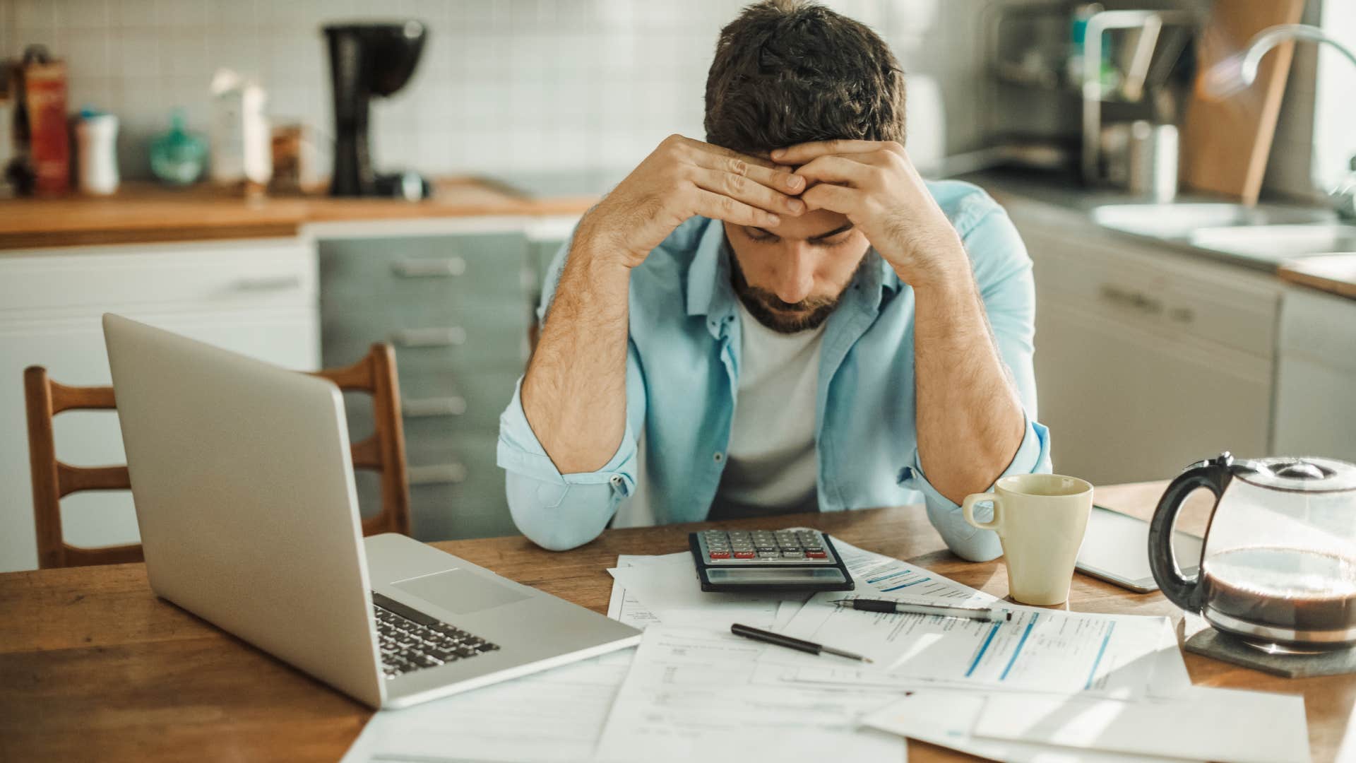 Stressed young man managing debt in kitchen