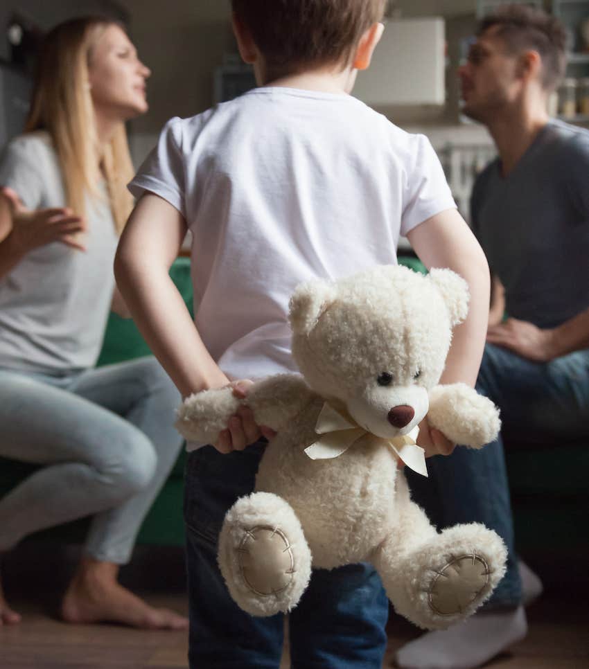 Child with teddy bear watches man and woman argue