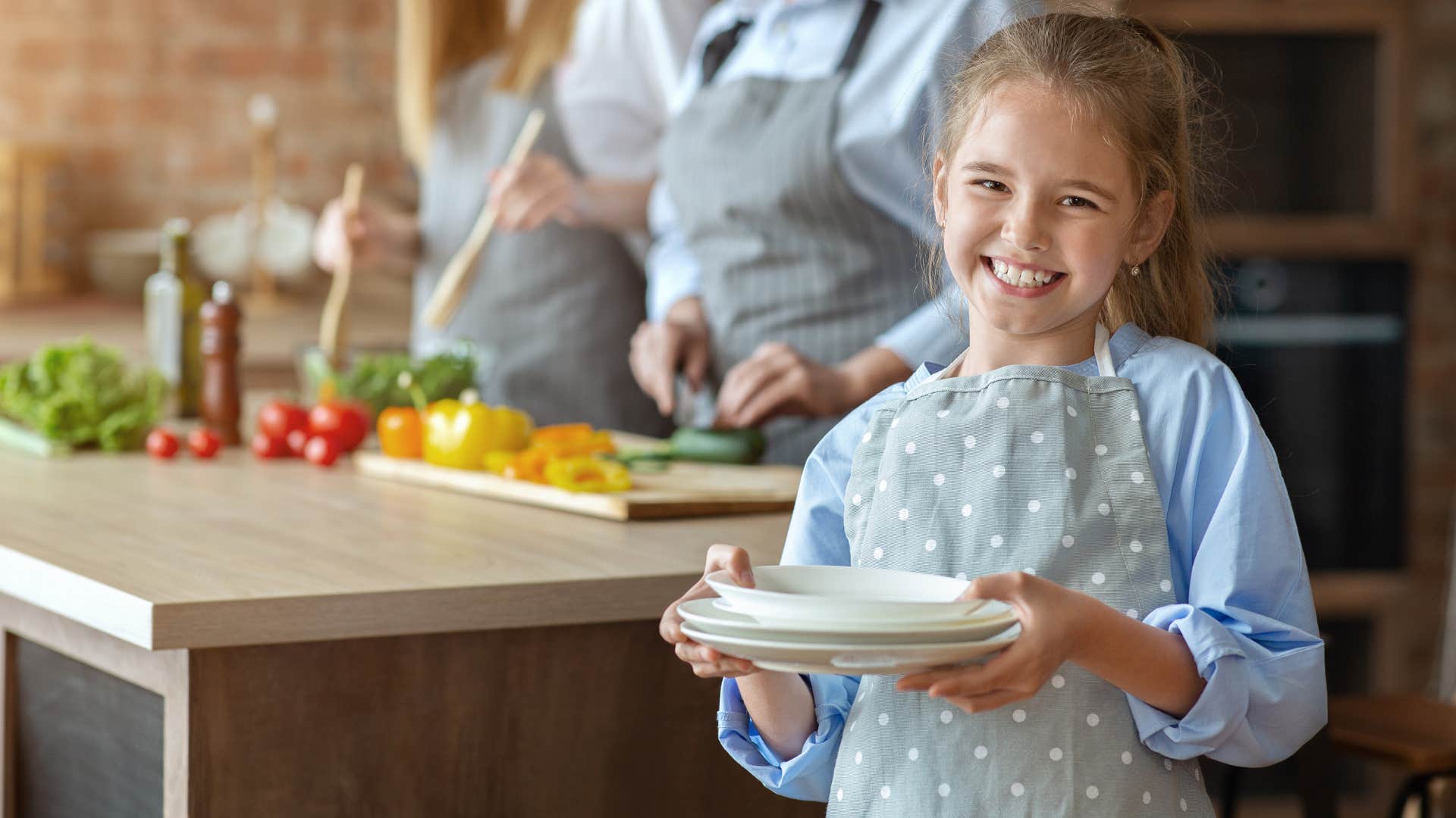 Little girl smiling and holding plates in the kitchen