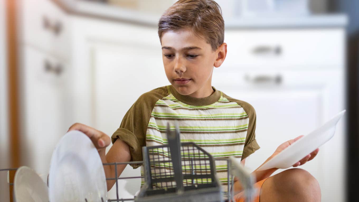 Little boy loading the dishwasher at home.