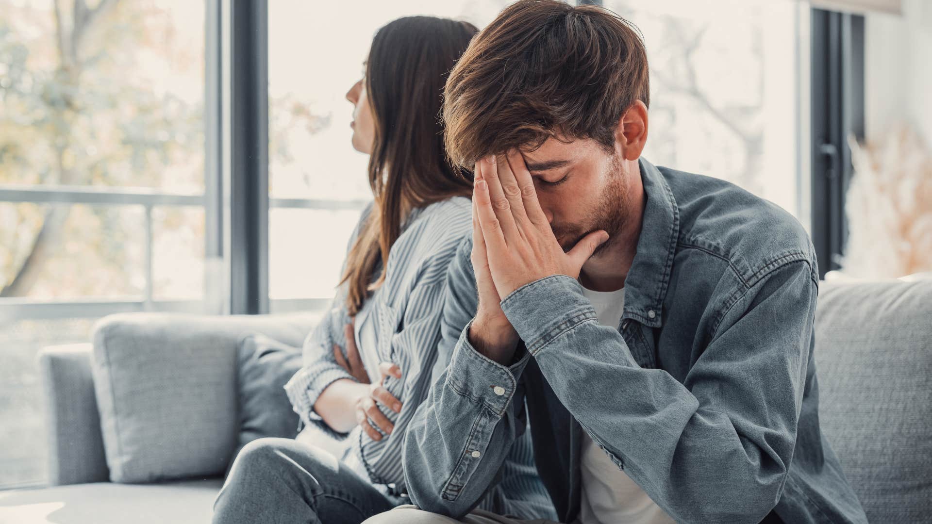 Upset man holding his head in his hands next to his partner.