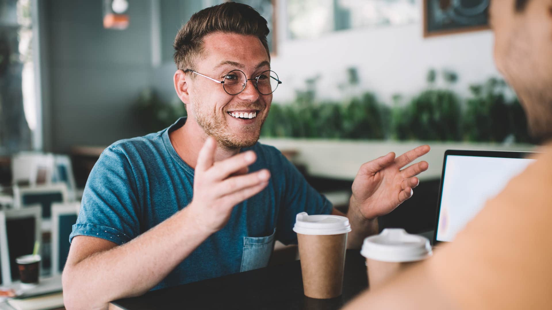 Man smiling and talking to his friend at a table.