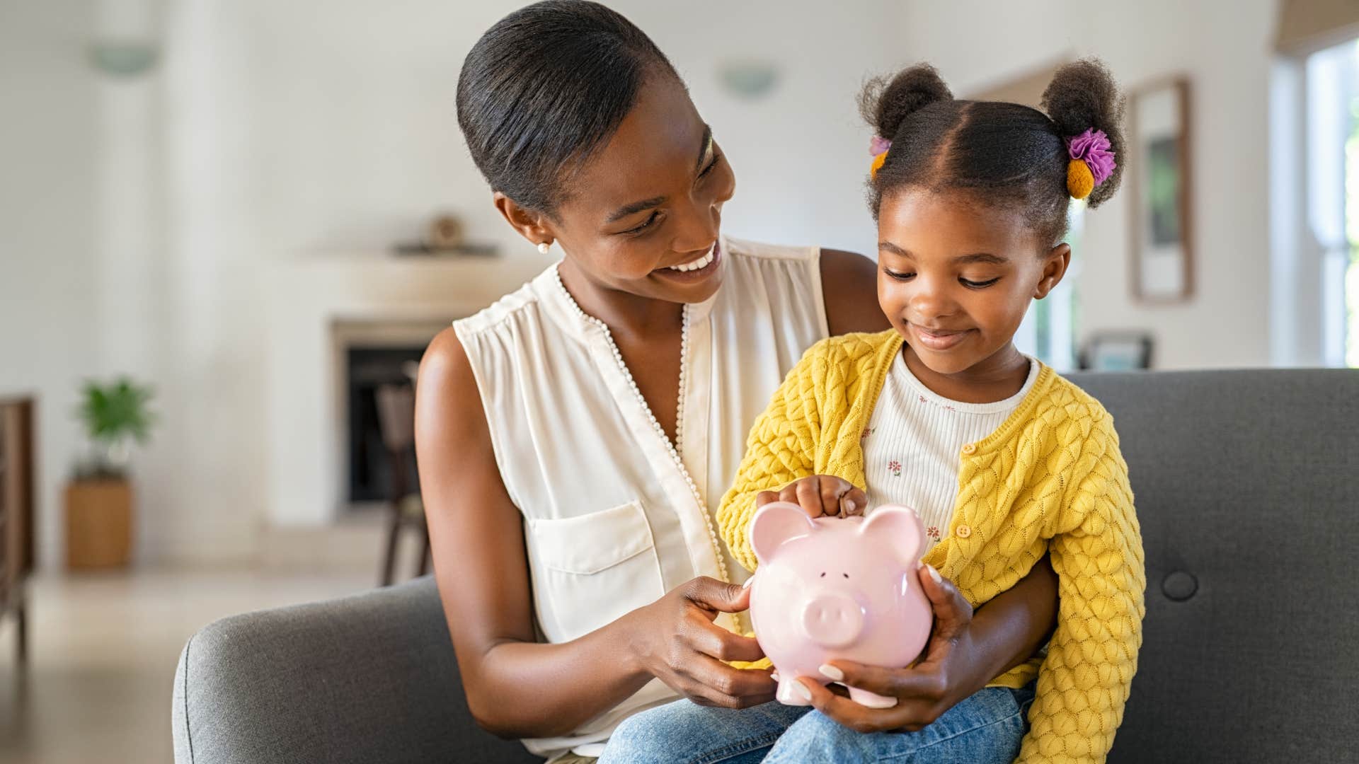 mother helping daughter put coins in piggy bank