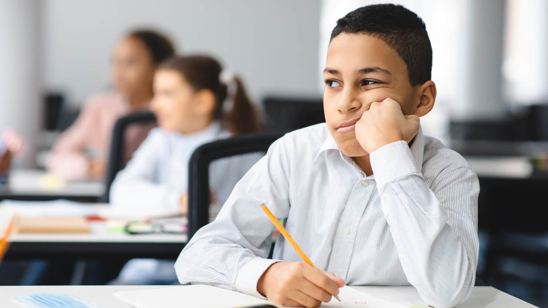 Little boy looking annoyed writing at his desk