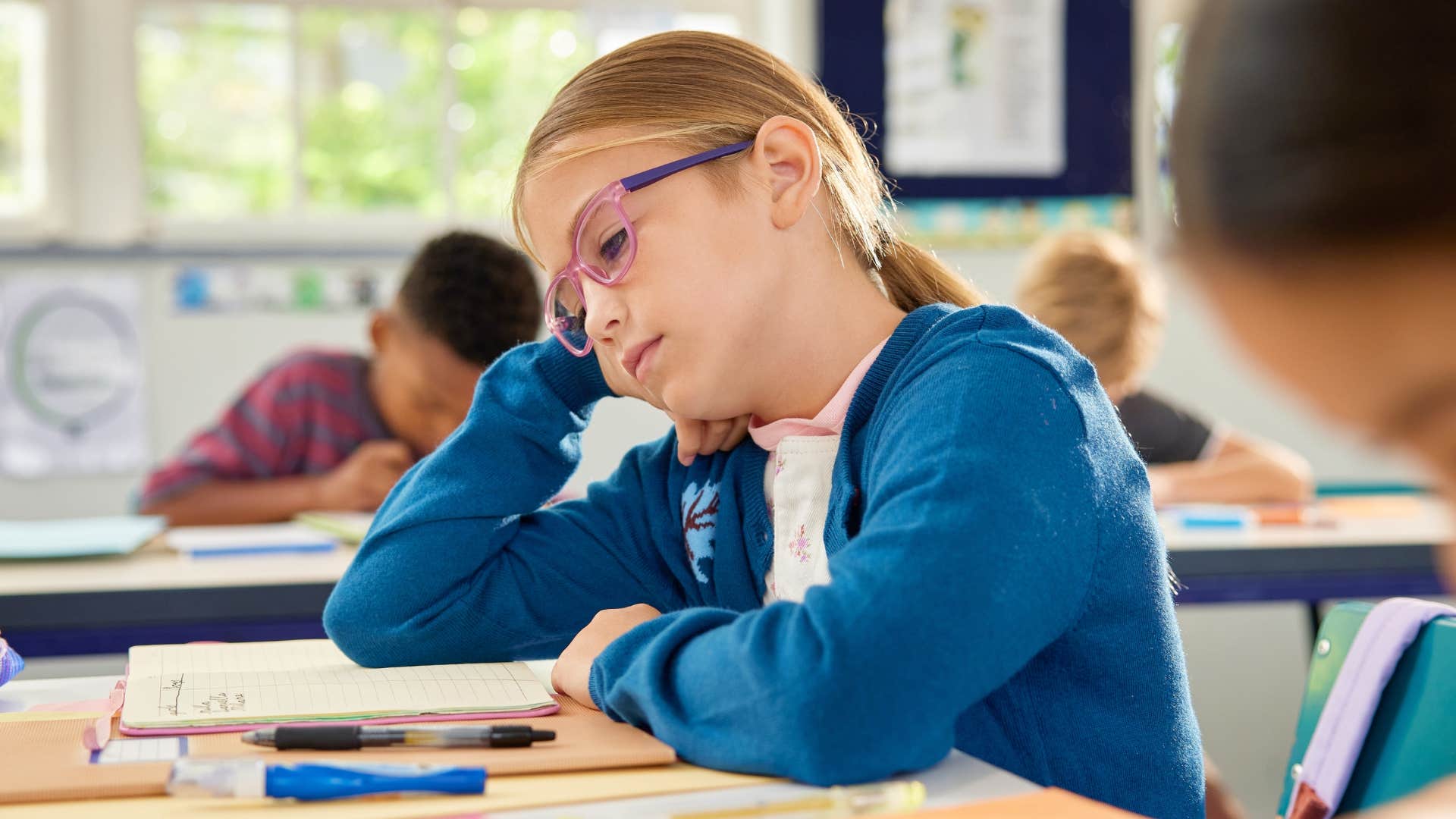 Little girl looking bored at her desk in a classroom