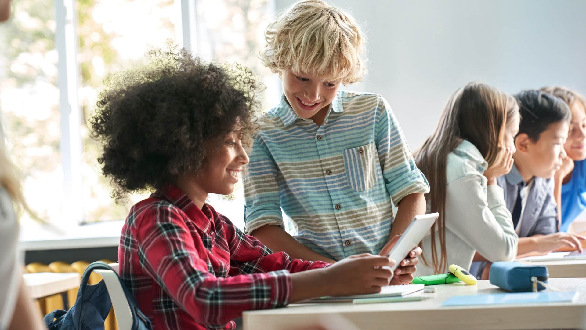 Two young classmates talking at a desk together