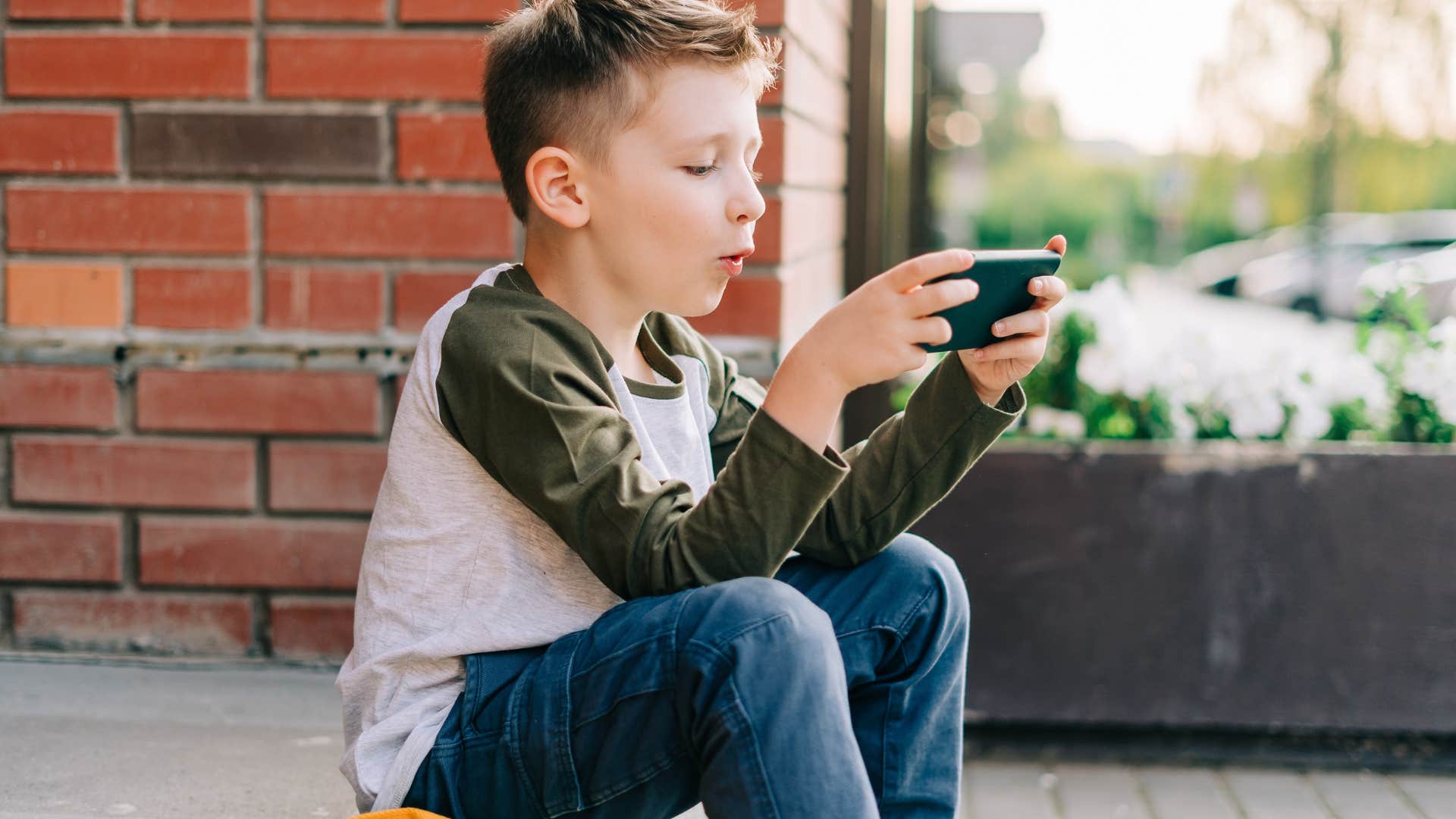 Little boy playing a game on his phone at school