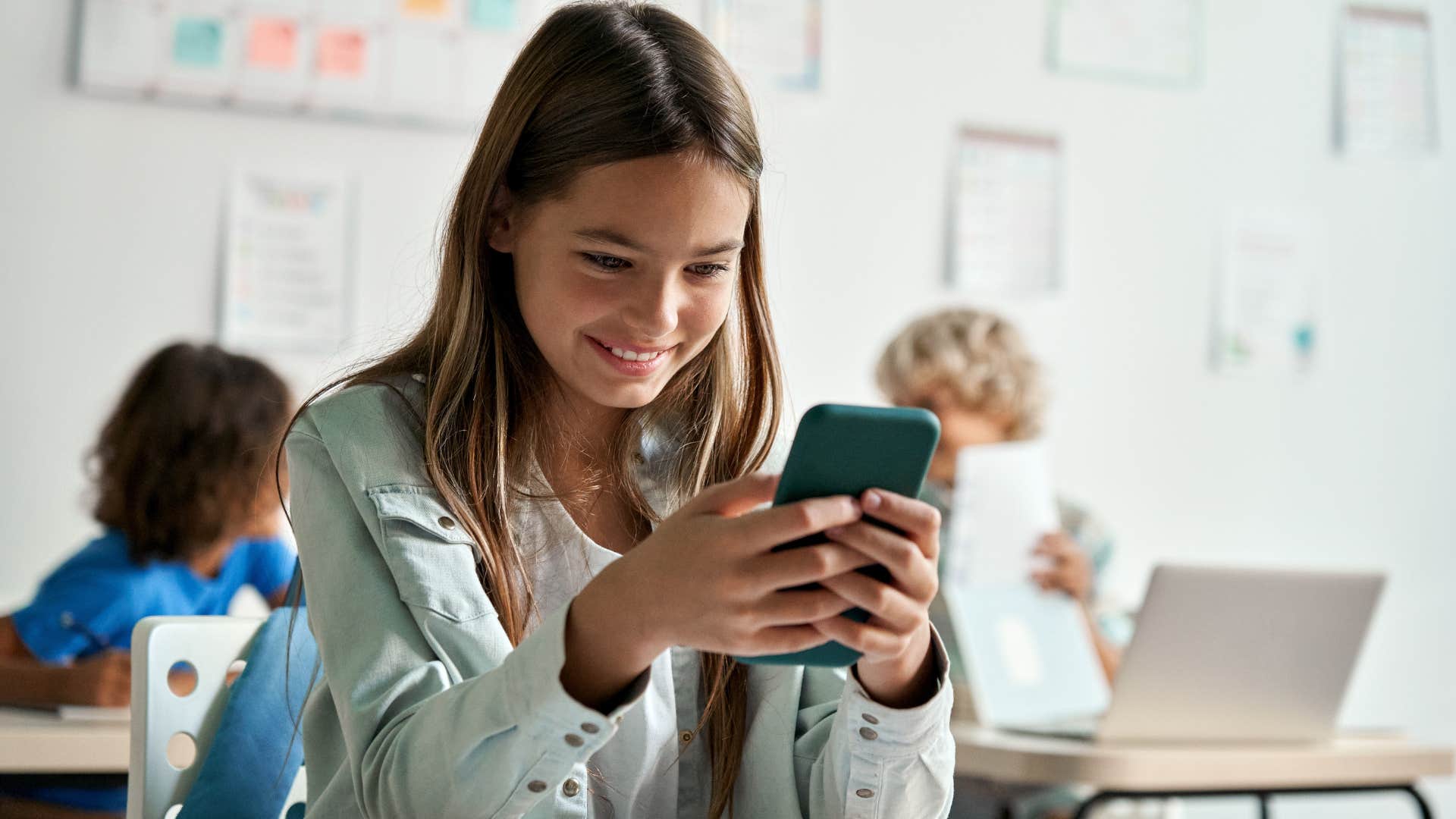 Young girl smiling at her phone in a classroom