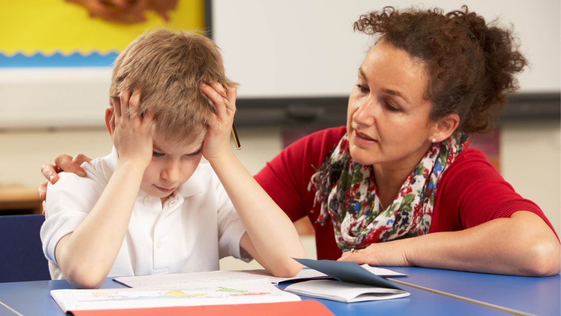 Teacher comforting a stressed young student at his desk