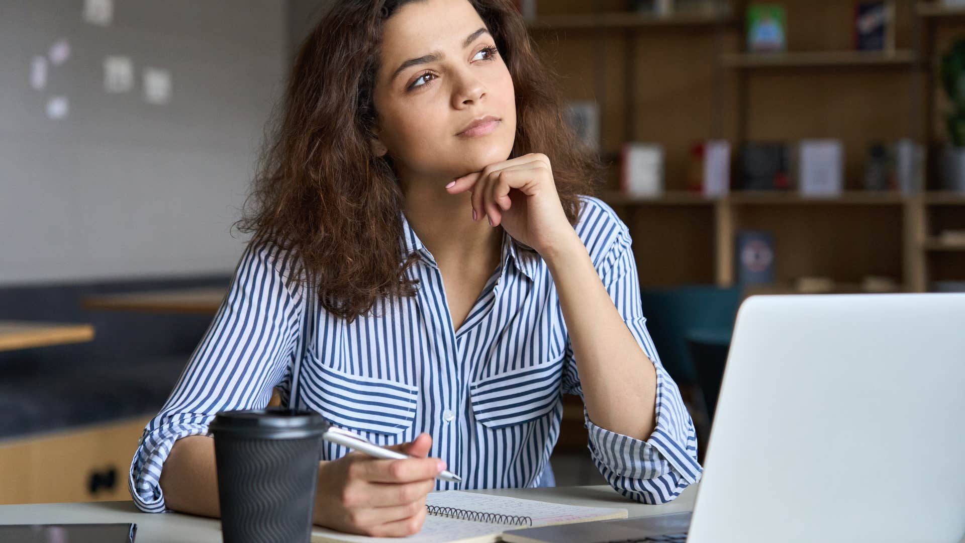 woman thinking while doing work on computer and with notebook