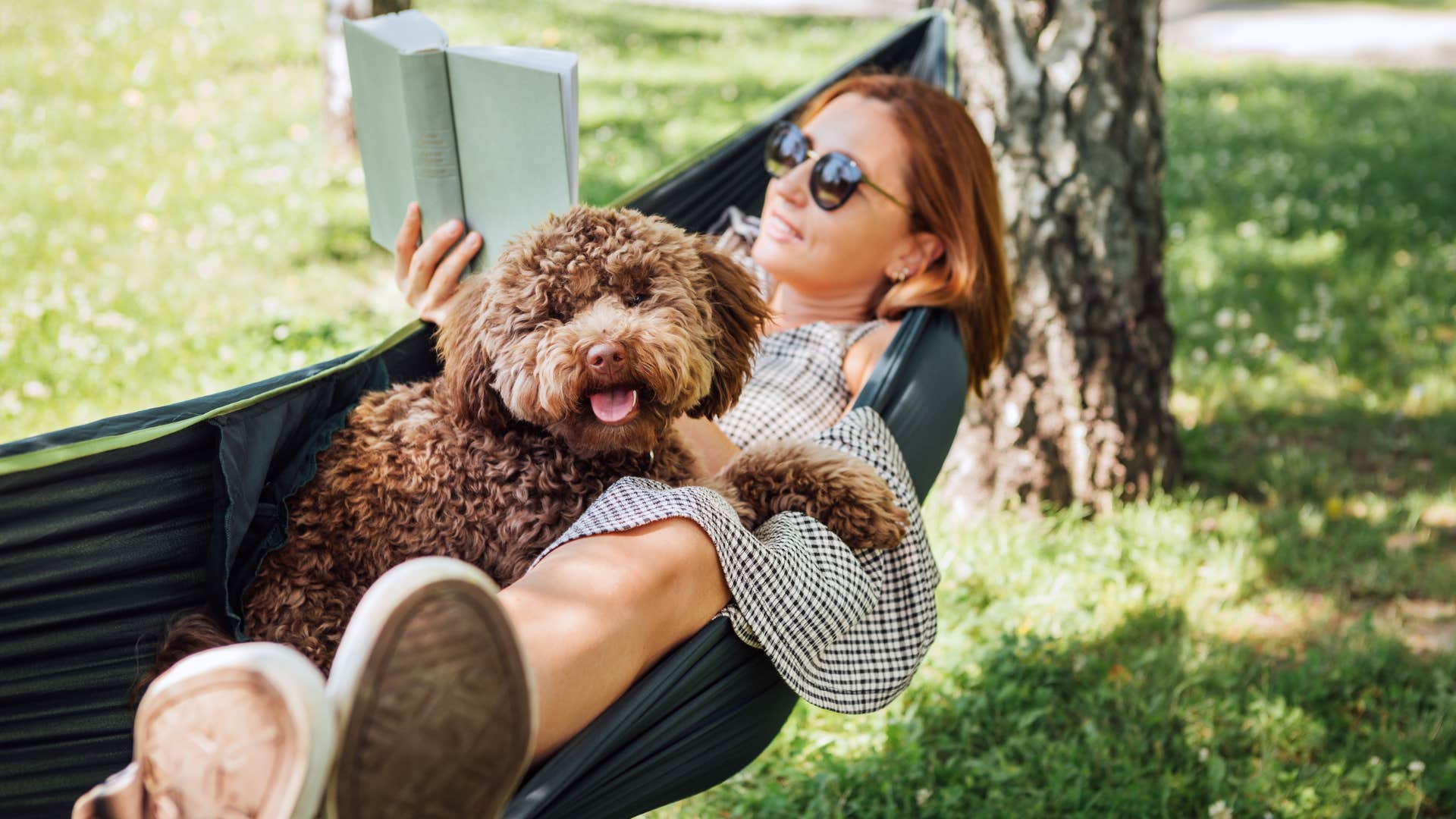 woman reading book laying in hammock with dog