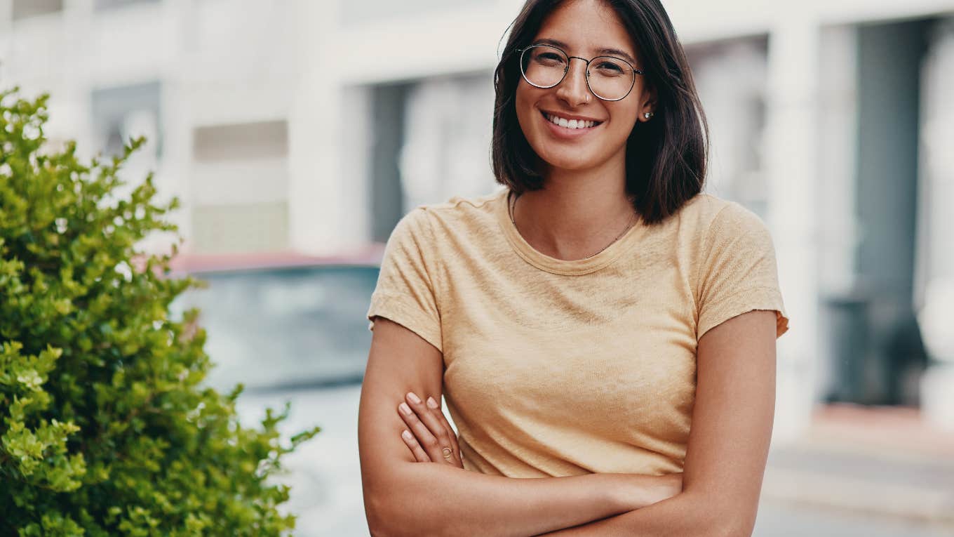 smiling, happy young woman standing next to plant outside