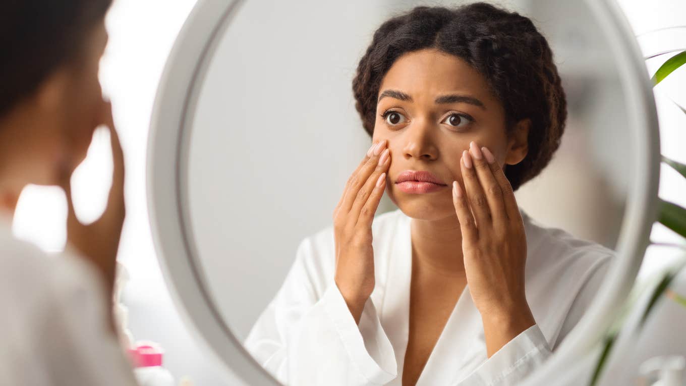 Millennial woman looking at aging skin in mirror. 