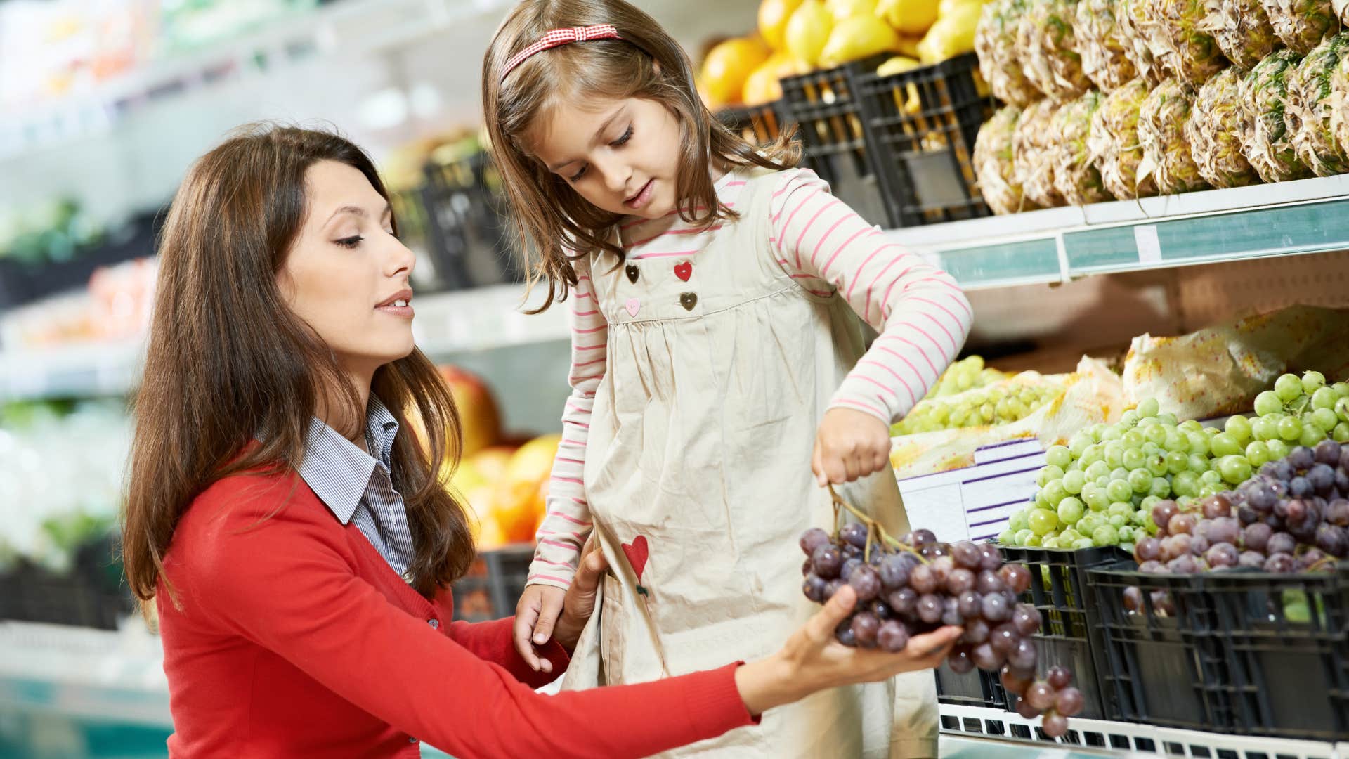 mom buying grapes with daughter at grocery store